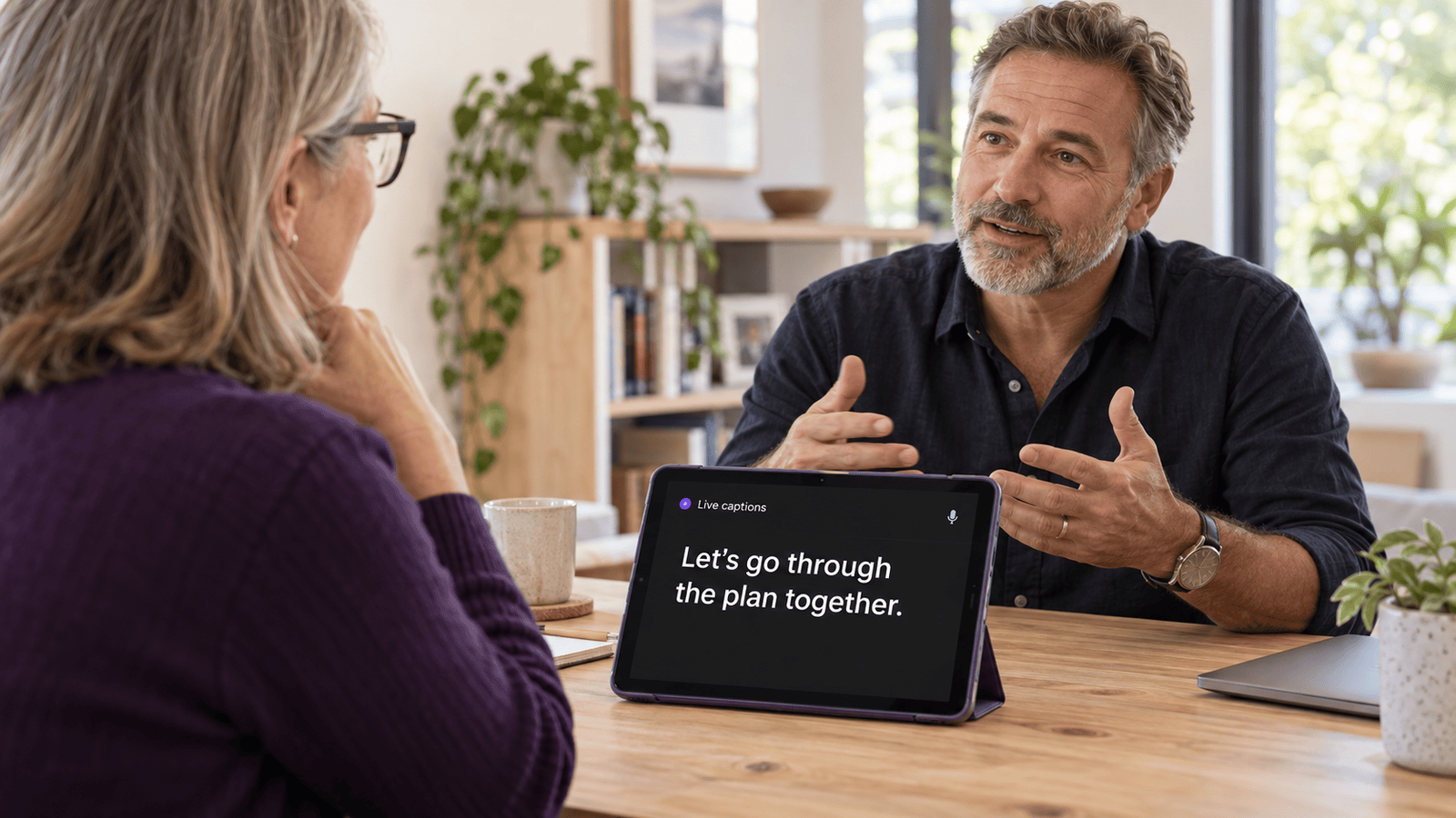 Two adults having a conversation with live captions displayed on a tablet.